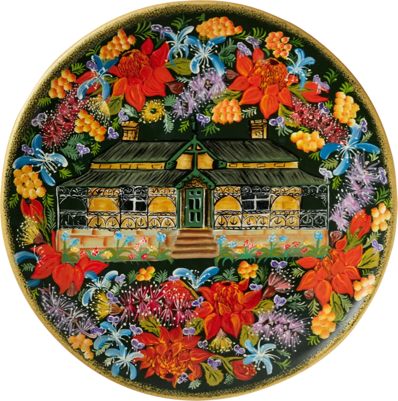 Hand-painted plate depicting a cottage framed by native flowers