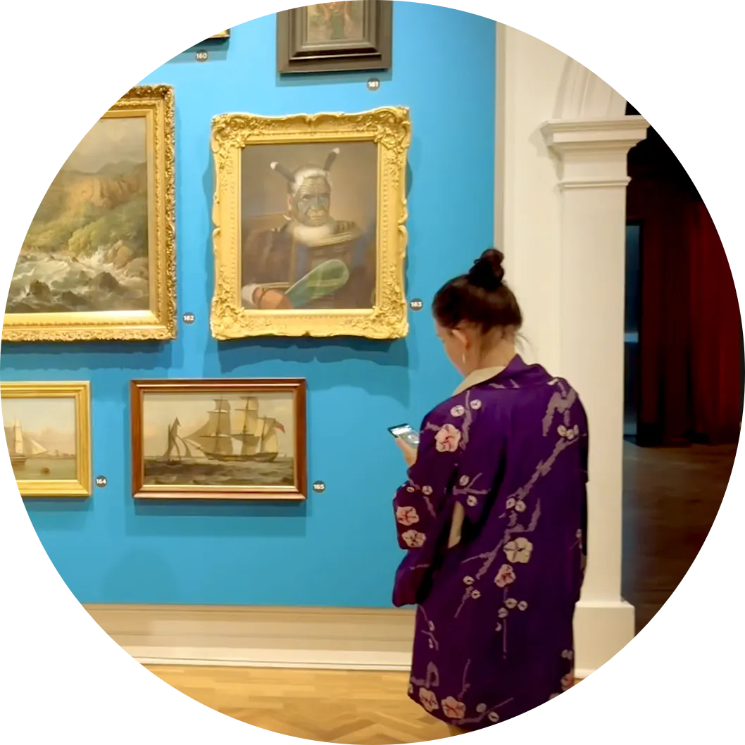 A visitor using an audio guide on her phone in front of the gallery wall