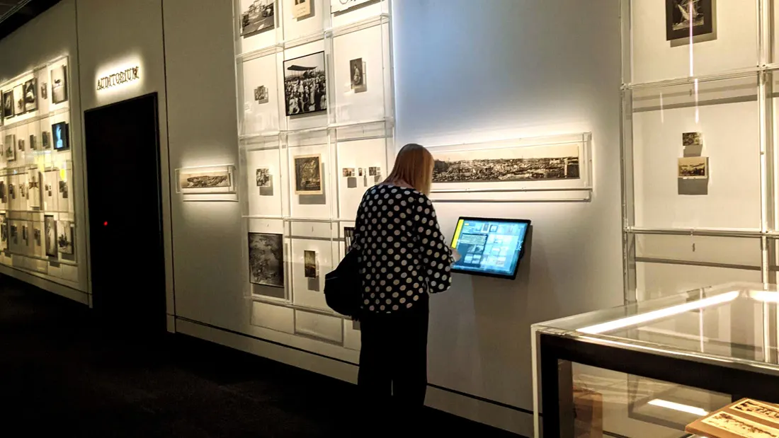 A visitor using a wall-mounted touchscreen kiosk beside the photography wall
