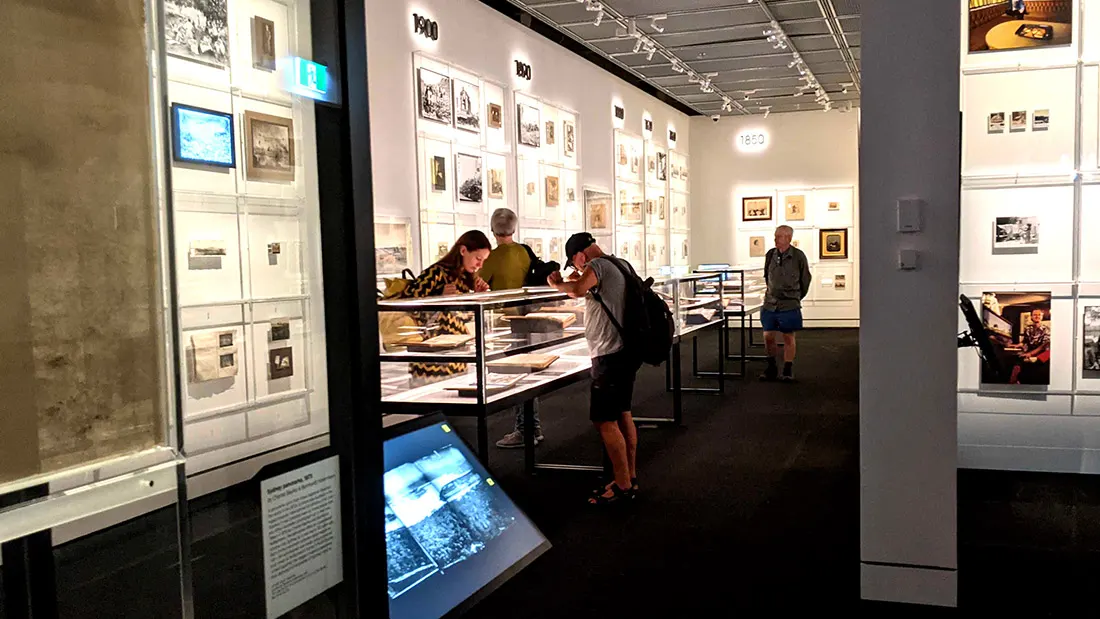 Visitors moving through the gallery, kiosks positioned along the display cases